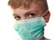 The face of a handsome white seven year old boy in a green protective surgical mask. Eyes with a gray iris. An excited look up and