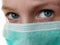 The face of a handsome white seven year old boy in a green protective surgical mask. Eyes with a gray iris. An excited look up and