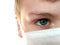 Face of a handsome white seven year old boy in a white protective surgical mask. Half face with eye with gray iris. Blonde hair.