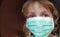 Face of a handsome white six year old girl in a green protective surgical mask. Face with eyes with gray iris. Blonde