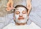 Face of laying man with cream mask, hands of beautician with brush
