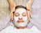 Face of laying man with cream mask, hands of beautician with brush