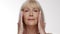 Face lifting concept. Studio portrait of positive senior caucasian lady making facial massage and smiling to camera