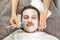 Face of man with cream mask, hands of beautician with brush