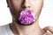Face of a man with a purple bud of a carnation in the mouth, a flower in the mouth of a man on a white background. Close-up. The