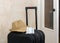 Face mask on a travelerâ€™s hand luggage next to a hat indoors at the door
