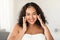Face massage. African american plus size woman touching her smooth flawless skin on cheeks and smiling at camera