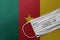 Face Medical Surgical White Mask with COVID-19 inscription lying on Cameroon National Flag. Coronavirus in Cameroon