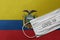 Face Medical Surgical White Mask with COVID-19 inscription lying on Ecuador National Flag. Coronavirus in Ecuador