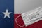 Face Medical Surgical White Mask with COVID-19 inscription lying on Texas State Flag. Coronavirus in Texas