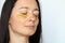 Face of middle aged woman applying golden collagen patches under eyes, on whitebackground. Beauty treatment