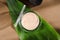 Face powder in round case top view on green leaf background. Fashion cosmetic, natural makeup product composition. Open compact