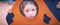 Face of small Caucasian girl looking through a hole in a play equipment outdoors. Orange background. Happy childhood