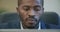 Face of successful African American businessman surfing Internet on laptop in office and smiling. Close-up portrait of