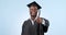 Face, thumbs up and black man with graduation, feedback and achievement on a blue studio background. Portrait, student