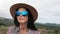 Face travel woman in sunglasses and straw hat putting on backpack at dramatic mountain sea landscape