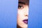 Face of young beautiful woman with a bright make-up and violet lips looks through a hole in violet paper.