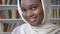 Face of young charming african muslim girl in hijab is watching at camera, religioun concept, booksheves on background