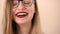 The face of a young emotional happy woman with long blonde hair and glasses. Happily laughs, looking at the camera