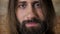 Face of young nice brunette man with beard is watching at camera, brick background