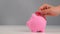 Faceless caucasian woman folds a small heart into a pink piggy bank on a white background. Love saving concept