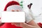Faceless caucasian woman in santa hat lying on bed at home, showing her phone