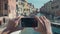 Faceless female hands taking photo of the picturesque venetian canal with her smartphone from edge of the bridge. Woman