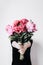 Faceless girl holds a bouquet of peonies on concrete wall background. Incognito flower delivery. Festive flowers concept