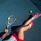 A faceless girl in a sports skirt sits on a tennis court and holds a rocket. Top view of female legs.