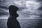 Faceless hooded person looking at horizon over sea water