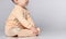 Faceless little toddler toddler child sits on the floor in the studio in a cotton yellow jumpsuit for baby