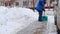 Faceless Male street worker with shovel removes snow from sidewalk in snowfall, back view. Slow motion