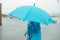 Faceless man in a blue protective raincoat and blue umbrella is walking down the street. selective focus