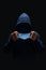 Faceless man in dark blue hoodie putting on blue surgical mask, face hidden in shadow