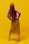 Faceless portrait of slim woman with long straight red hair wearing retro fashion outfit in action over yellow studio