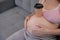 Faceless pregnant woman in 3rd trimester holding a coffee glass on her belly.