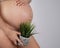 Faceless pregnant woman holding a plant. Metaphor for epilation of the bikini area.