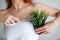 Faceless red-haired Caucasian woman wrapped in a white terry towel shears a potted plant with scissors. Armpit hair