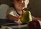 Faceless toddler, a little boy or girl sits at the table and reaches for the pear. Matte shadows, sunset color