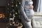 Faceless womans pregnant belly in velvet grey evening dress closeup in cozy home interior on Christmas tree background