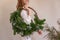 Faceless young woman holds in hands asymmetrical green Christmas wreath made from natural materials