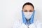 Facial portrait of a female doctor in a dressing gown, respiratory mask and gloves, looking at the camera. On white background