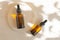 Facial serum in amber glass bottles with dropper lids on round wooden stand. Flat lay, white background with floral shadow.