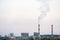 Factory chimneys against the gray autumn sky. Utopian landscape background. White toxic smoke is coming from a huge pipe.