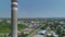 Factory high chimney stack. Camera ascending. Town in the back. Sunny. Aerial drone shot.