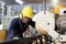 A factory mechanic is using a chainsaw to cut copper pipes. An expert technician is inspecting industrial machinery in a steel