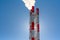 Factory red white metallic chimney with steam or smoke against a blue sky