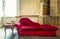 Faded grandeur. Chaise longue in red velvet with books and table, vintage, retro abandoned house and furniture.