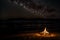 The fading glow of a beach bonfire under the starlit sky