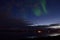 Faint aurora borealis over calm fjord at night with lights